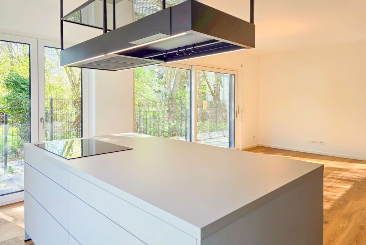 Modern kitchen with a white island and built-in cooktop, large glass doors to a green outdoor garden. (informative)