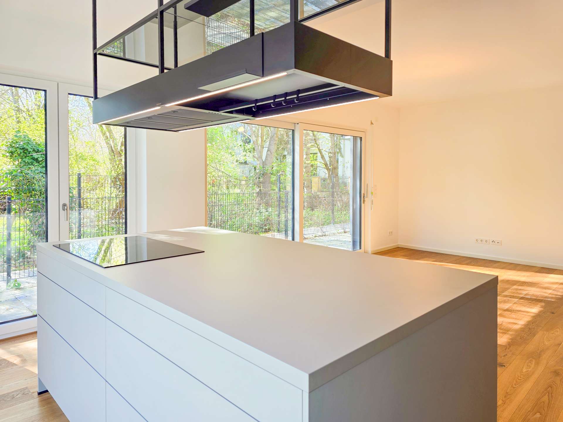 Modern kitchen with a white island and built-in cooktop, large glass doors to a green outdoor garden. (informative)