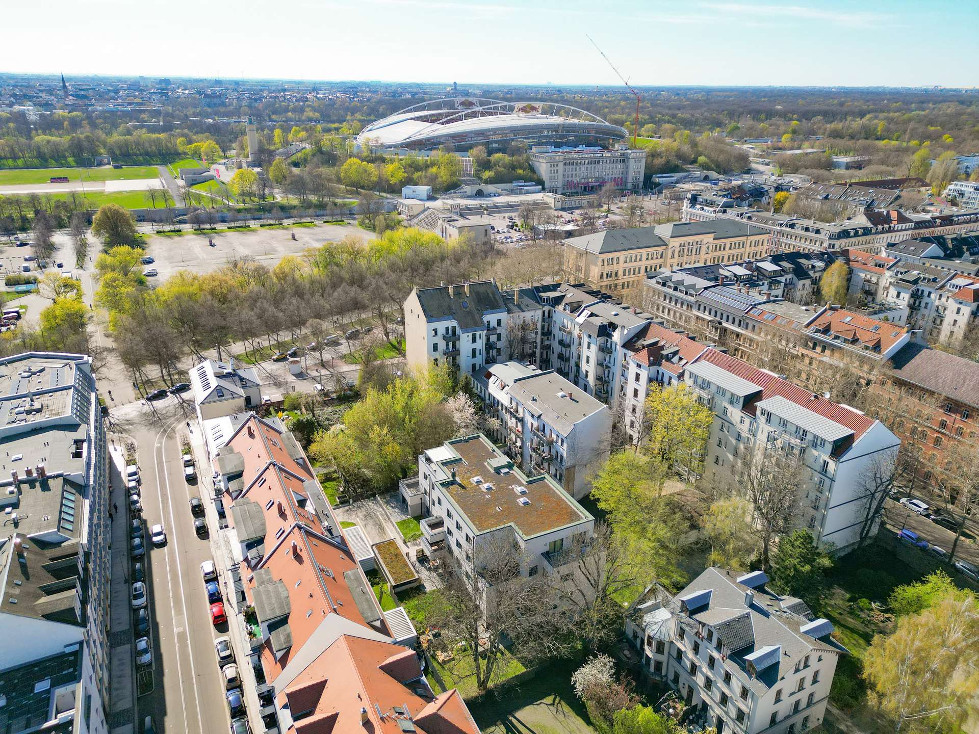 Aerial view of a city neighborhood with red-roofed buildings and a large futuristic stadium in the distance.