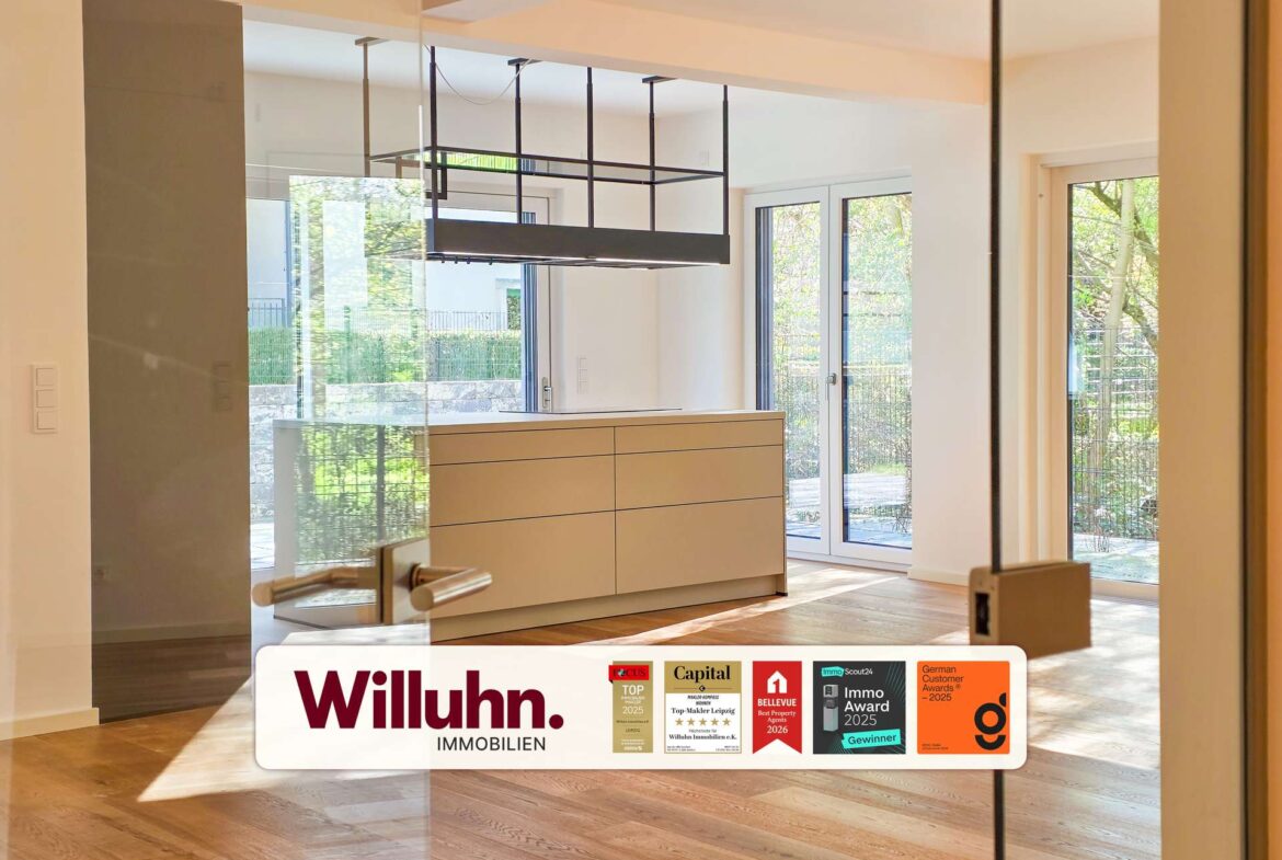 Modern showroom interior featuring beige cabinetry, glass walls, and large windows with natural light; Willuhn Immobilien branding in the foreground.