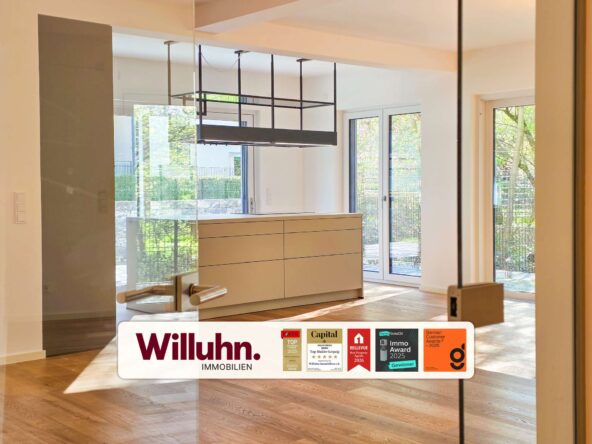 Modern showroom interior featuring beige cabinetry, glass walls, and large windows with natural light; Willuhn Immobilien branding in the foreground.