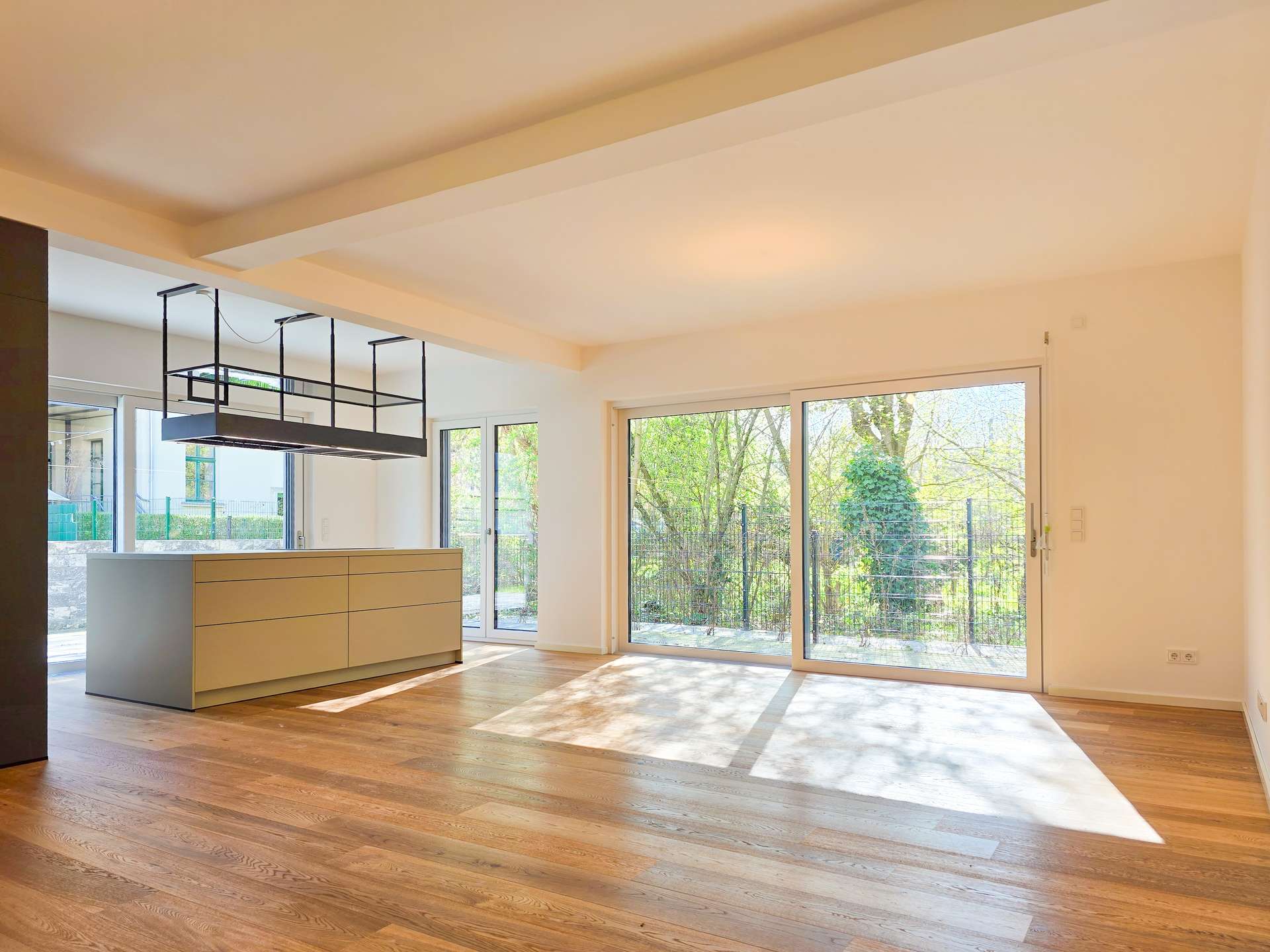 Open-plan kitchen and living area with warm wood flooring, white cabinetry, and large sliding glass doors overlooking a garden.