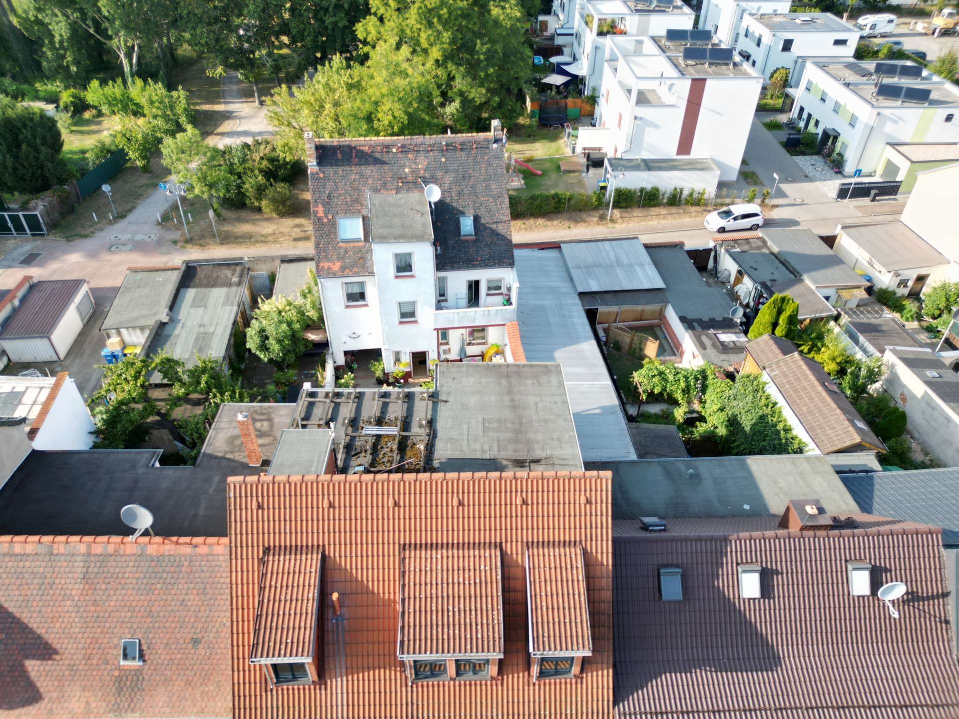 Aerial view of a residential area with red-tiled roofs and white facades among green trees and narrow streets.
