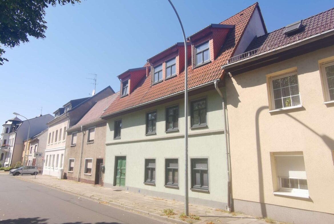 Row of pastel-colored townhouses along a sunny street with red-tiled roofs and dormer windows under a clear blue sky.