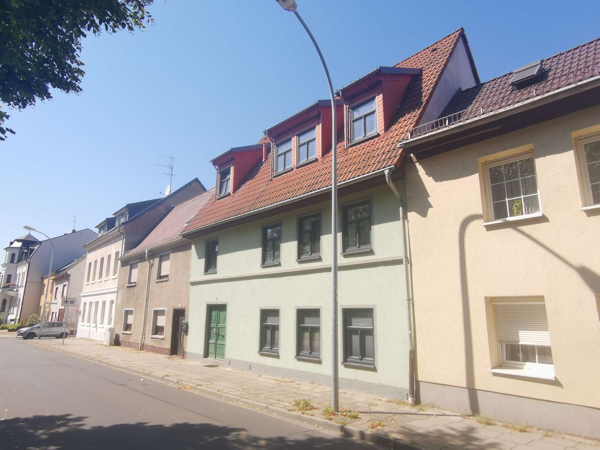 Row of pastel-colored townhouses along a sunny street with red-tiled roofs and dormer windows under a clear blue sky.