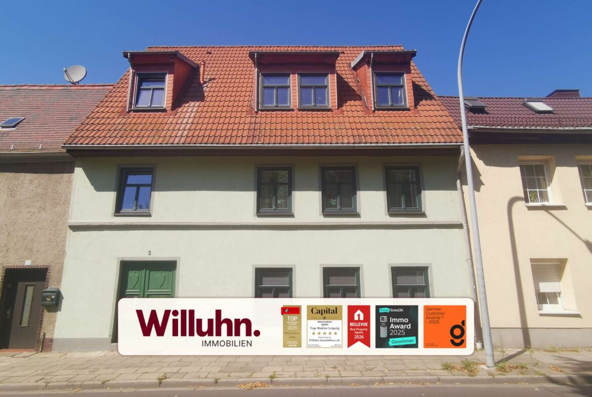 Front of a pale building with a red tiled roof and a large Willuhn Immobilien sign displaying award logos on the sidewalk in front of it.