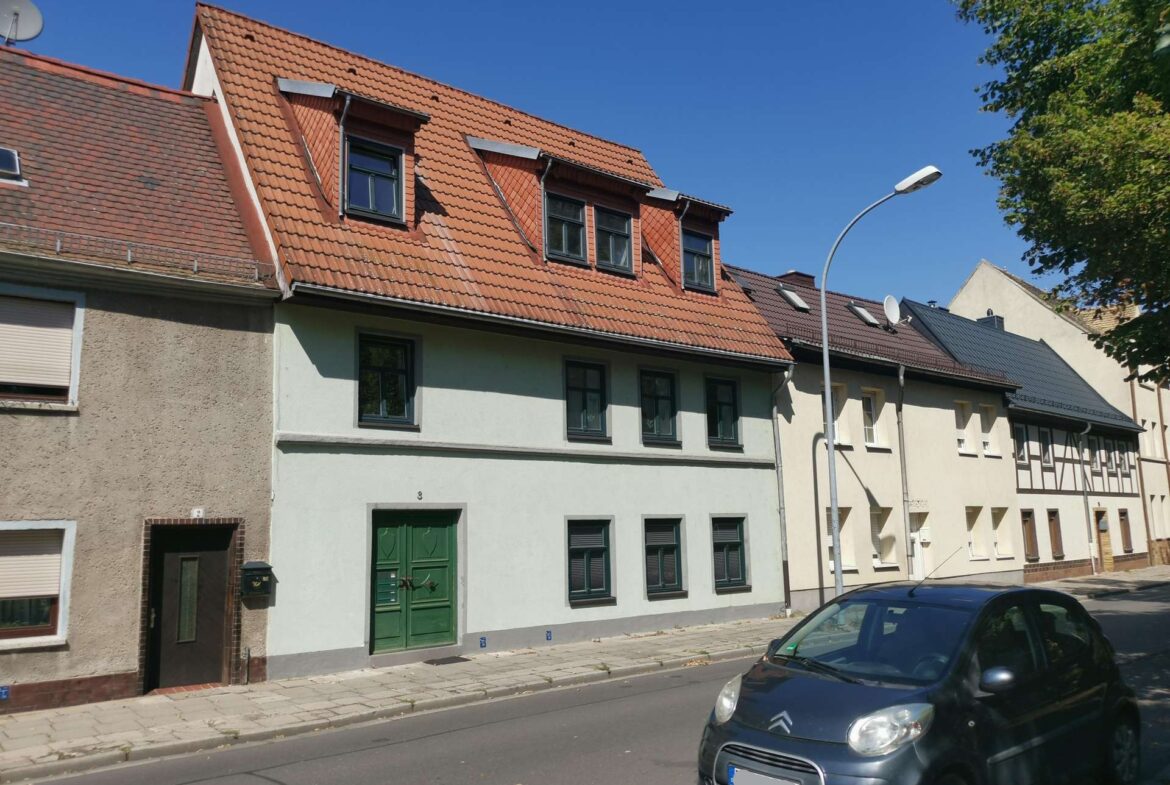 Row of European houses with red tiled sloped roofs, dormer windows, and a green front door under a clear blue sky.
