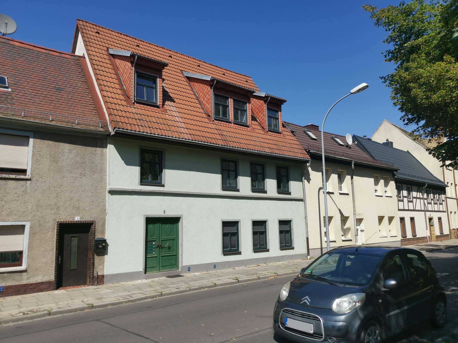 Row of European houses with red tiled sloped roofs, dormer windows, and a green front door under a clear blue sky.