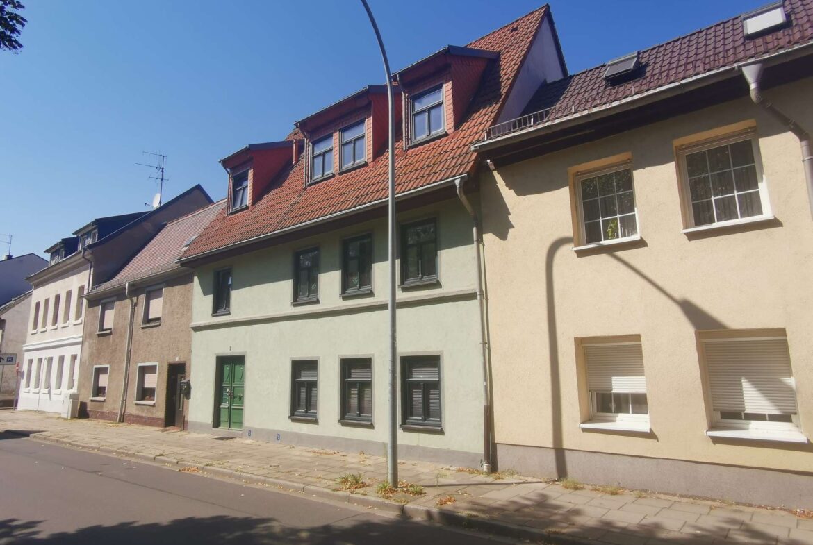 Row of pastel-colored townhouses with red-tiled roofs on a sunny street.