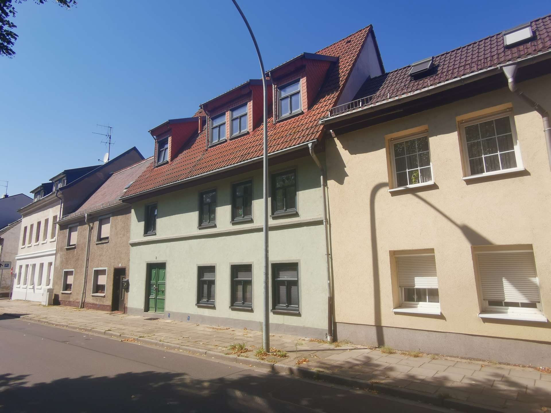 Row of pastel-colored townhouses with red-tiled roofs on a sunny street.