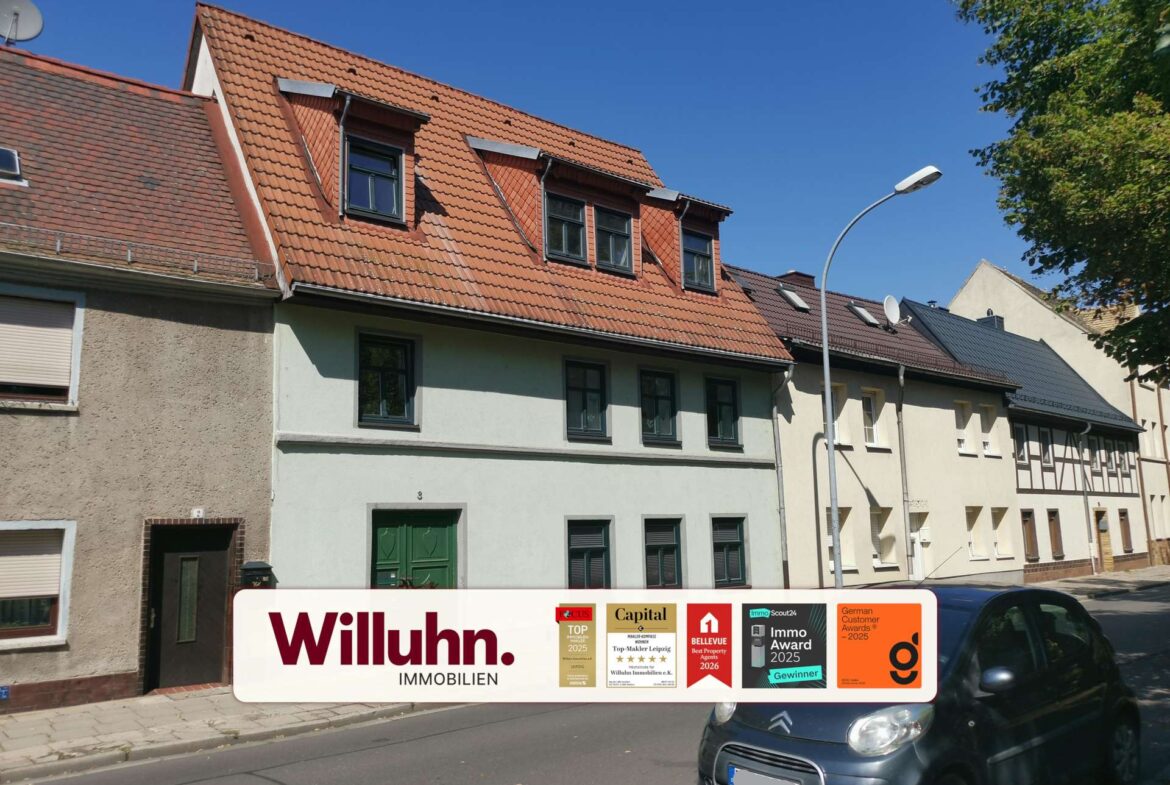 Residential street with red-tiled roofs and a large Willuhn Immobilien advertising sign in the foreground; awards stickers are visible on the sign, a car parked on the right.