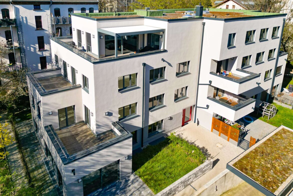 Aerial view of a modern white apartment building with glass balconies and rooftop terraces viewed from above.