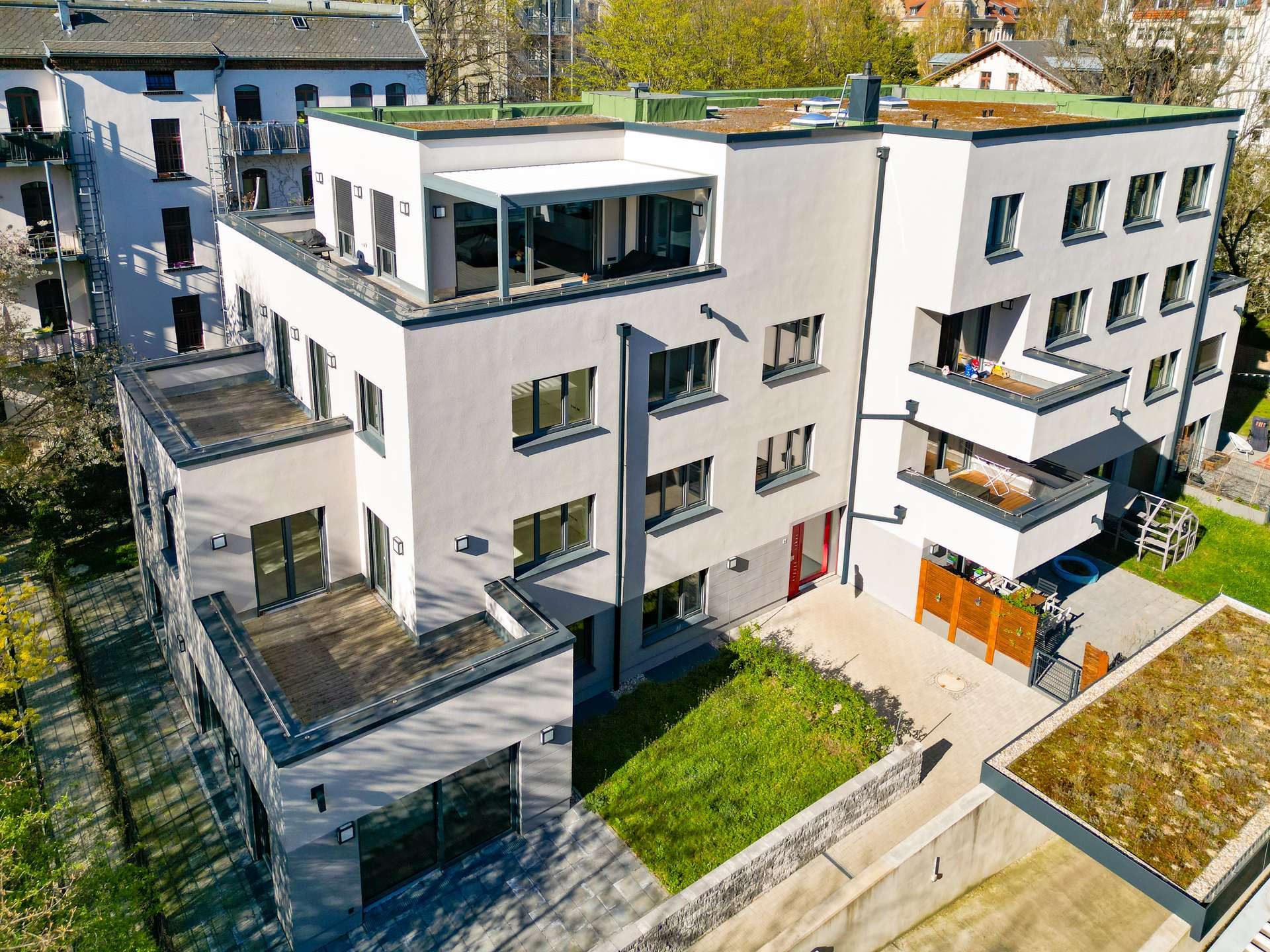 Aerial view of a modern white apartment building with glass balconies and rooftop terraces viewed from above.