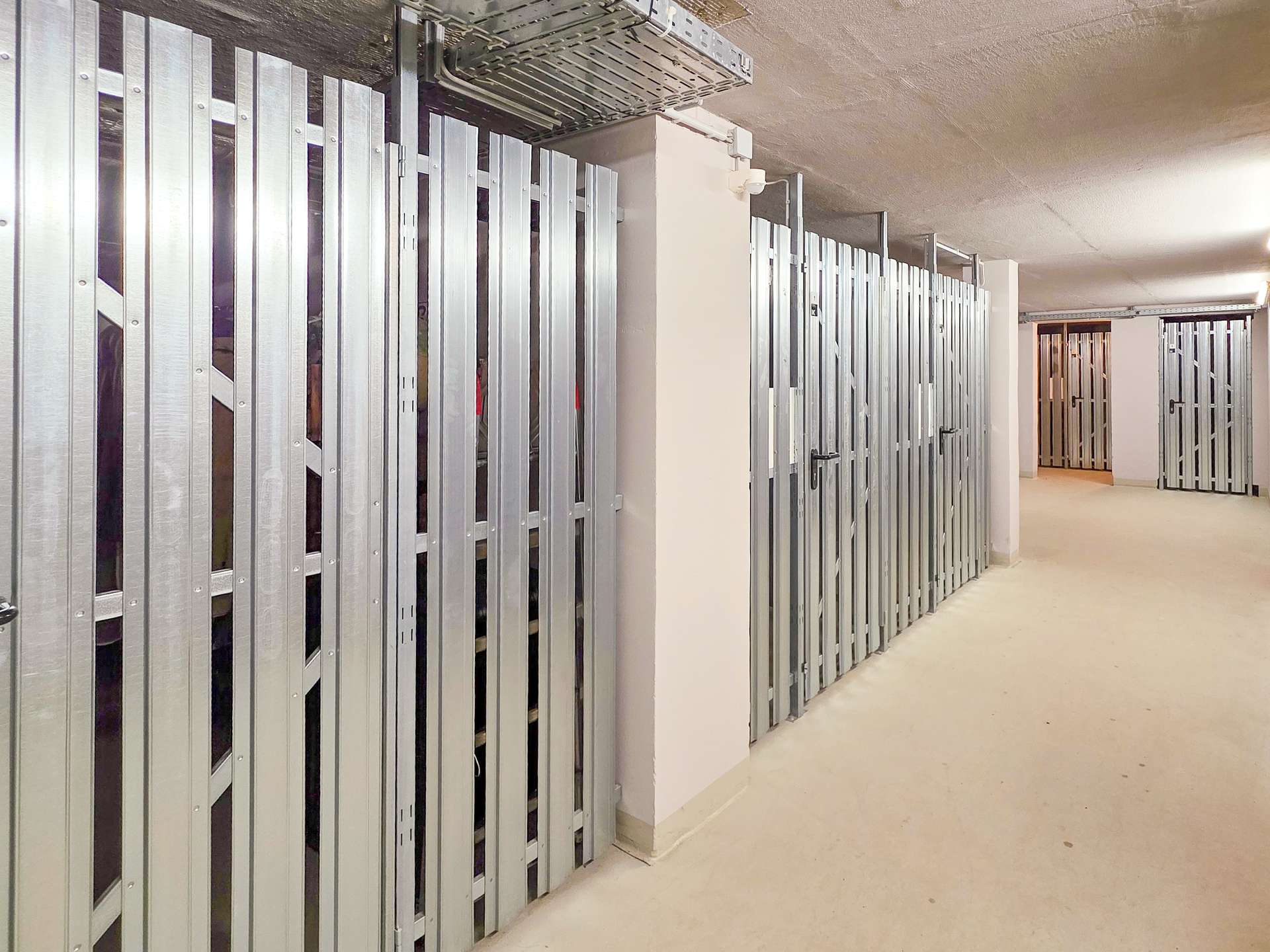 Long hallway of a storage facility with silver metal lockers lining the walls on both sides.