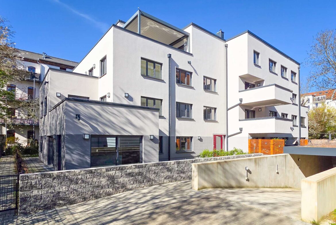 Modern white apartment building with multiple windows and balconies under a clear blue sky.