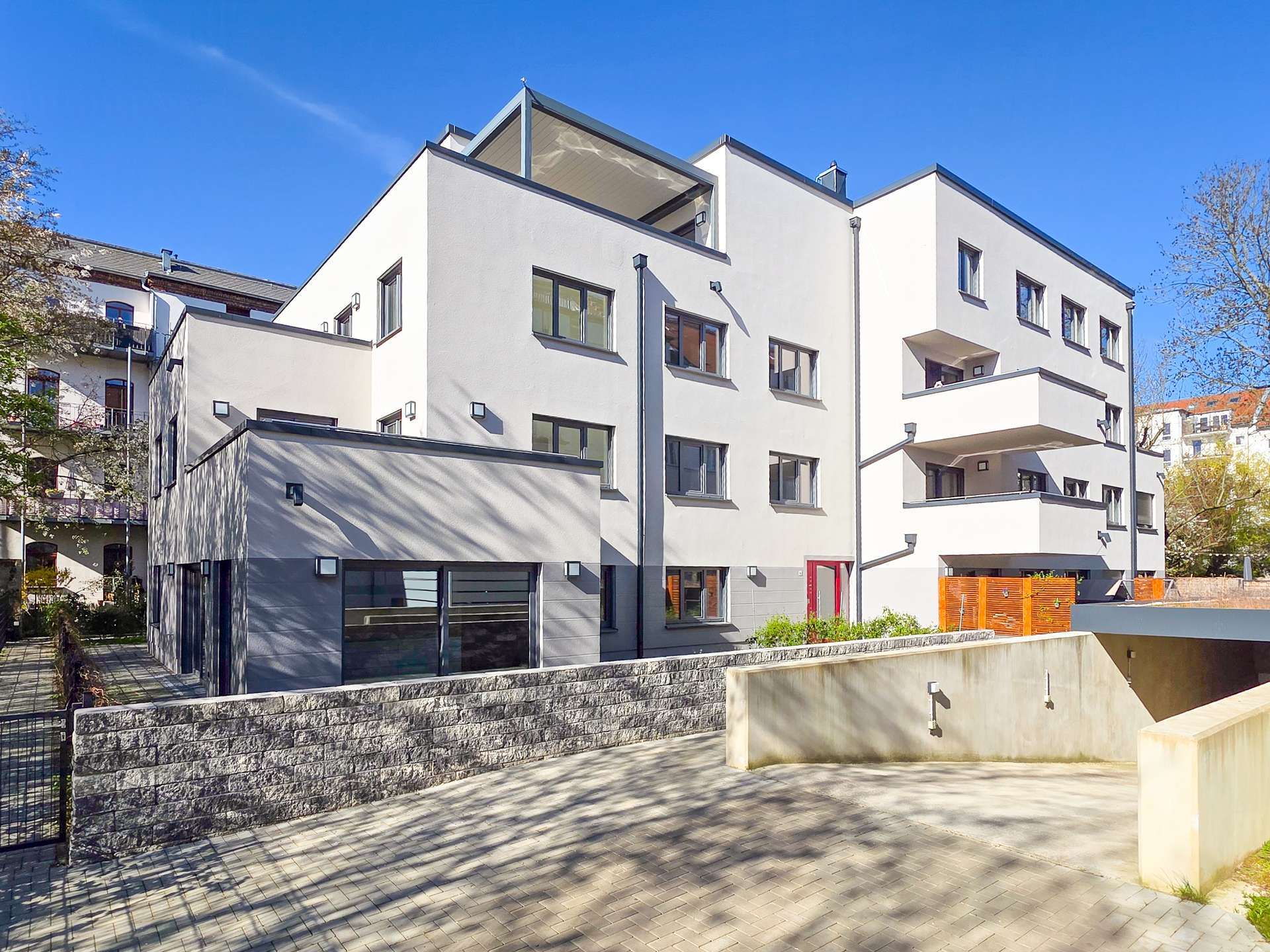 Modern white apartment building with multiple windows and balconies under a clear blue sky.