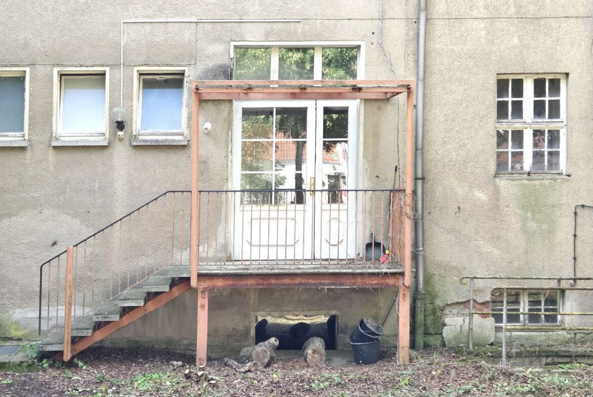 Back of a weathered gray apartment building with an orange metal staircase leading to a white door.