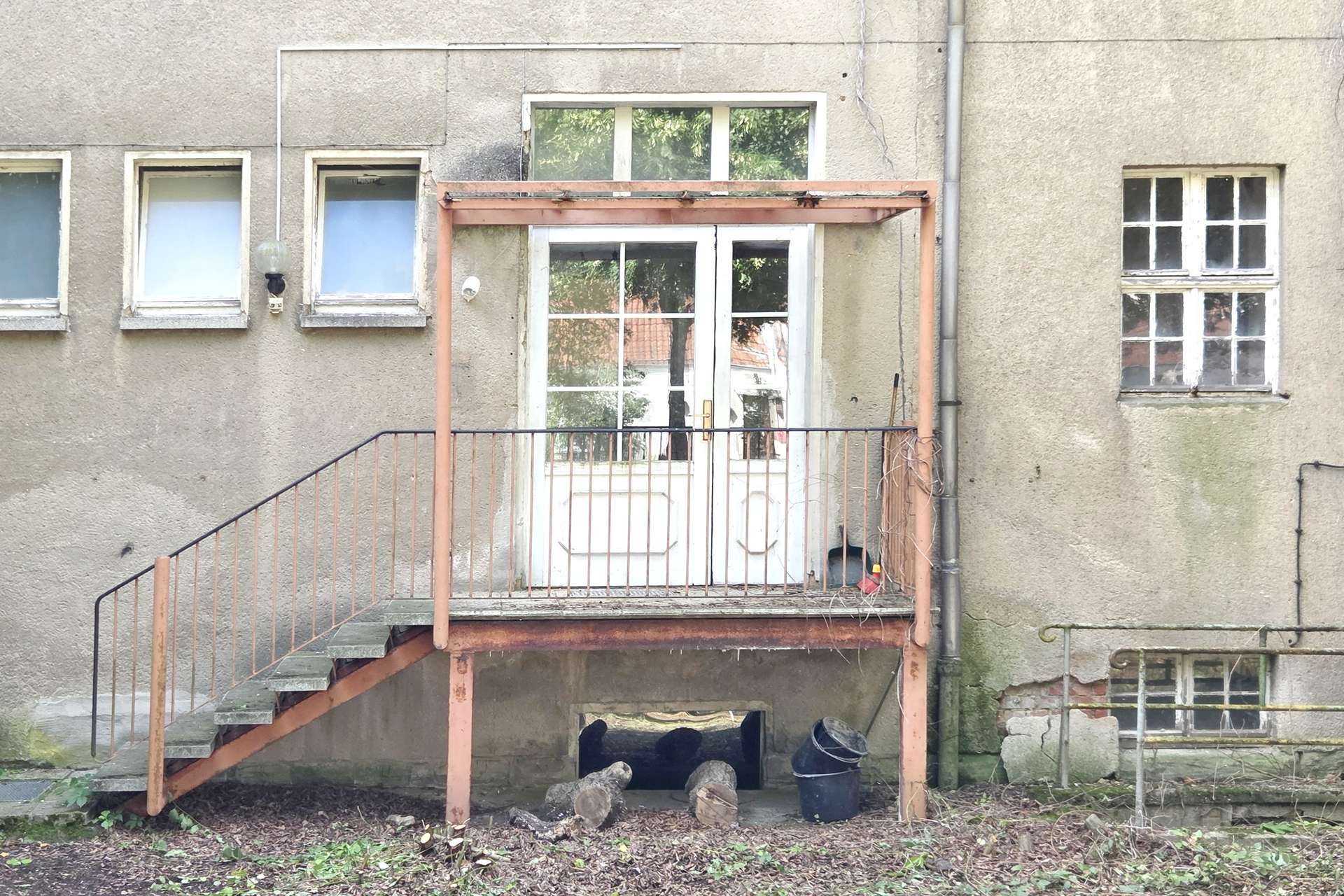 Back of a weathered gray apartment building with an orange metal staircase leading to a white door.