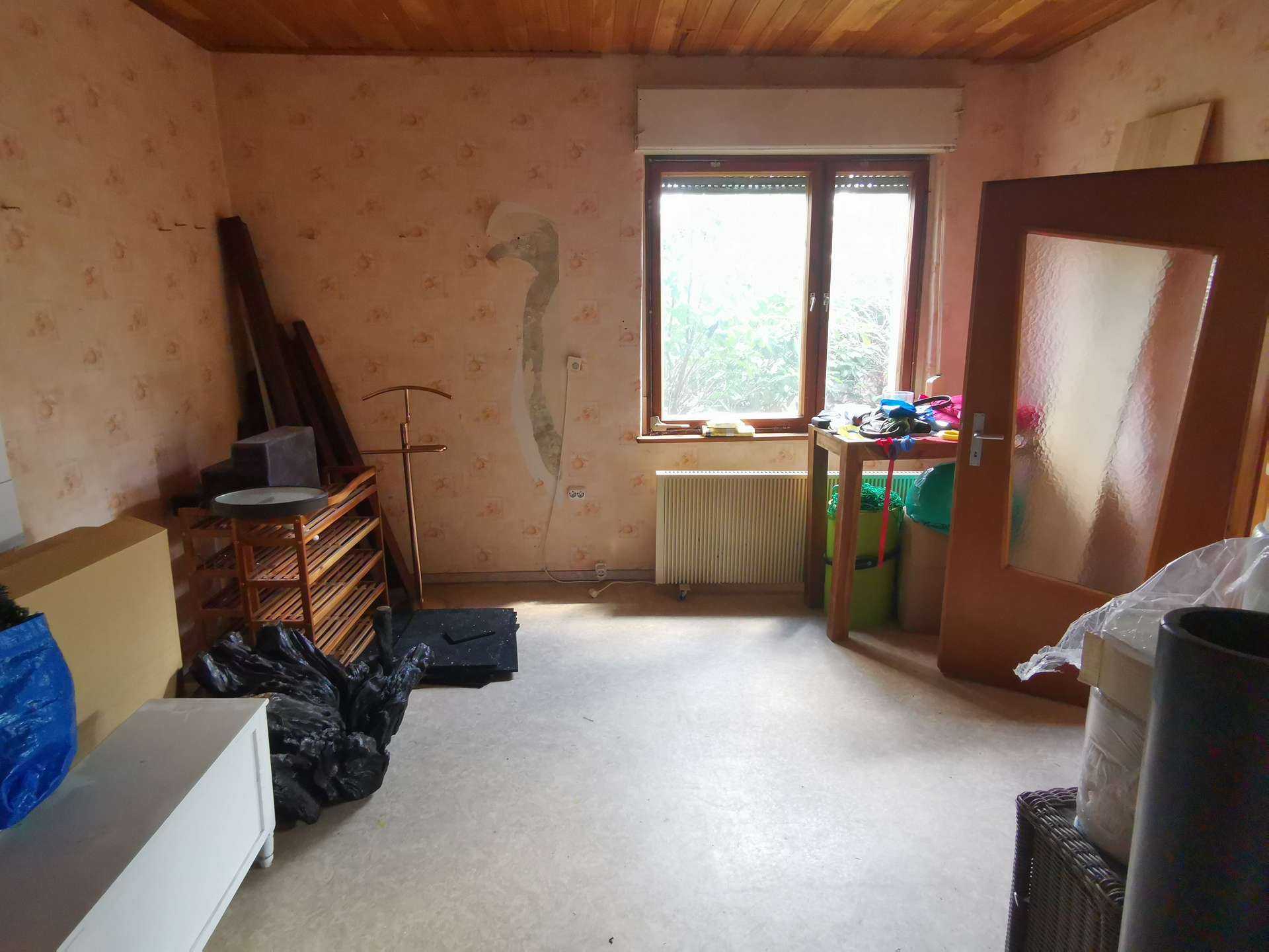 Cluttered storage room with a window, radiator, and shelves filled with tools and bags.