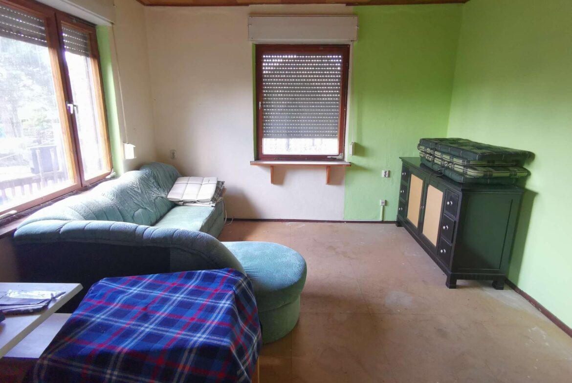 Living room with a blue plaid sofa against a light wall and a green accent wall, window blinds, and a dark cabinet with cushions on top.