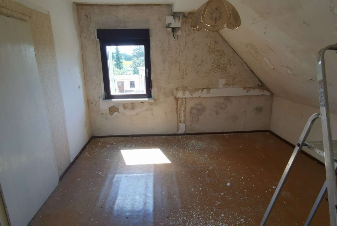 Attic renovation scene: small room with peeling walls, a single window, and a metal ladder leaning inside, sunlight on the floor.