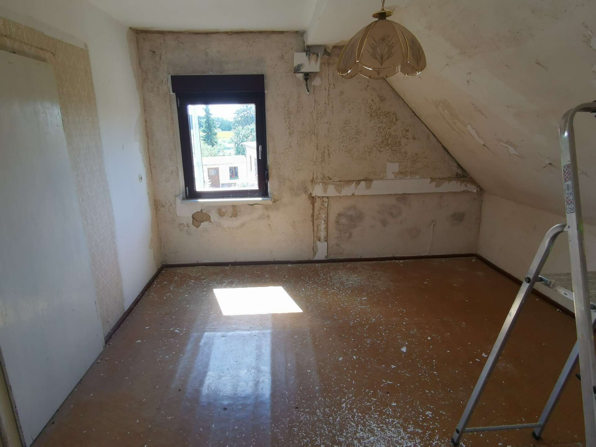 Attic renovation scene: small room with peeling walls, a single window, and a metal ladder leaning inside, sunlight on the floor.