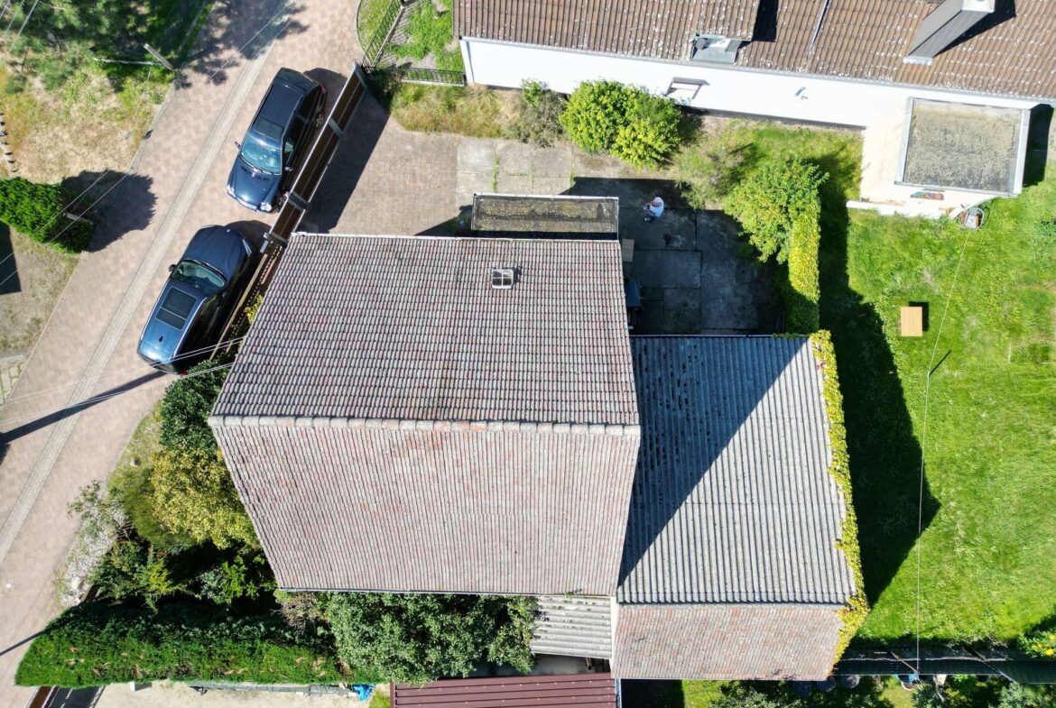 Aerial view of a residential area showing tiled rooftops, driveways, and small green yards with trees and hedges