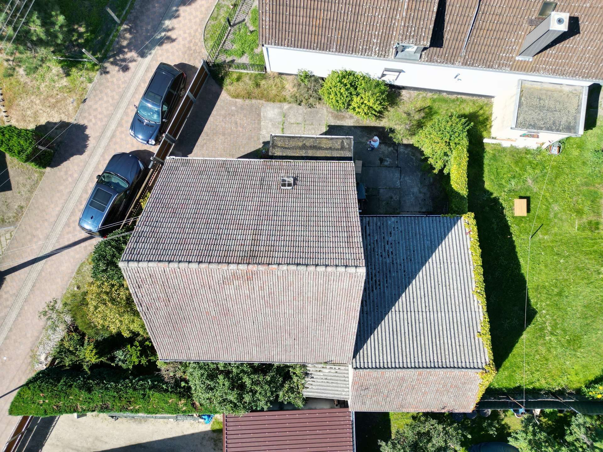 Aerial view of a residential area showing tiled rooftops, driveways, and small green yards with trees and hedges
