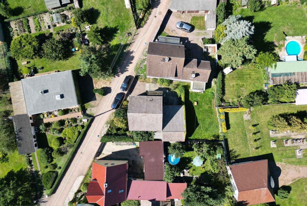 Aerial view of a suburban neighborhood with a curved road, red-tiled roofs, and green gardens on both sides.