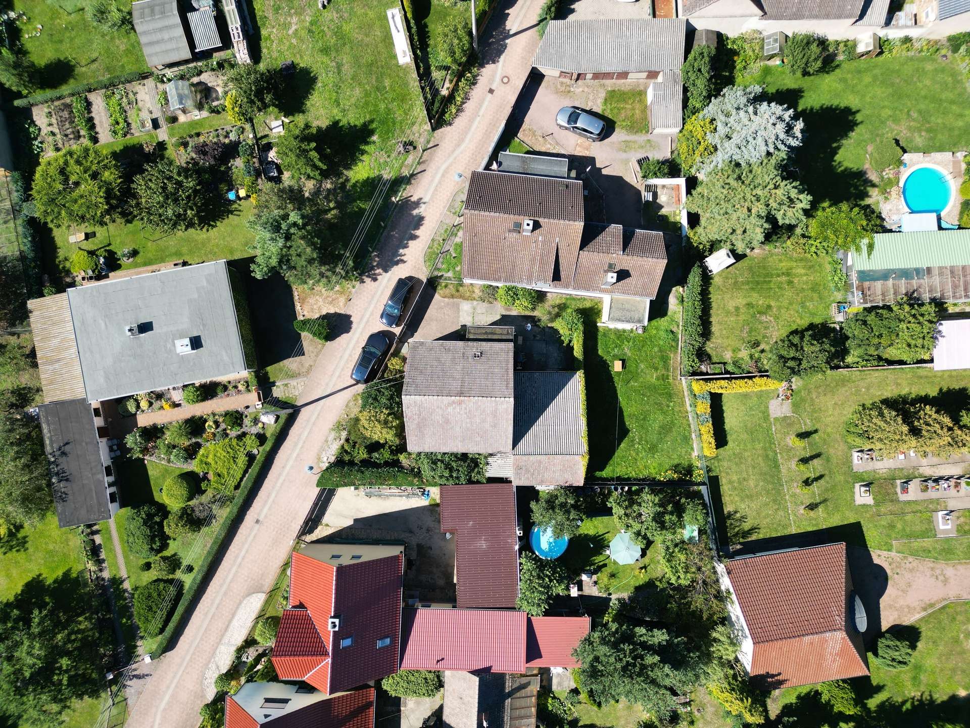 Aerial view of a suburban neighborhood with a curved road, red-tiled roofs, and green gardens on both sides.