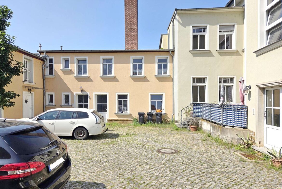 Cobblestone courtyard between pastel yellow apartment buildings with several windows and parked cars.