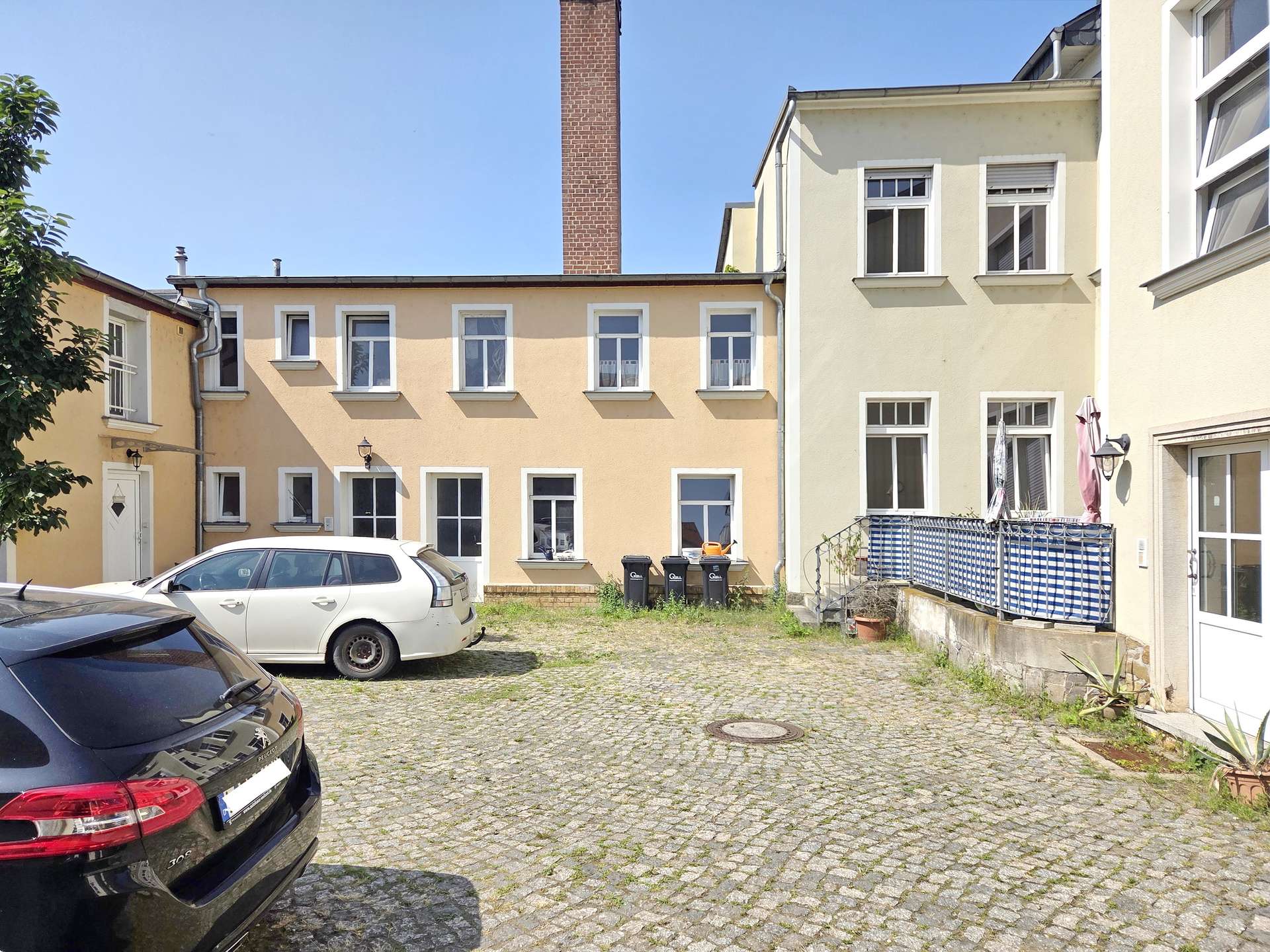 Cobblestone courtyard between pastel yellow apartment buildings with several windows and parked cars.