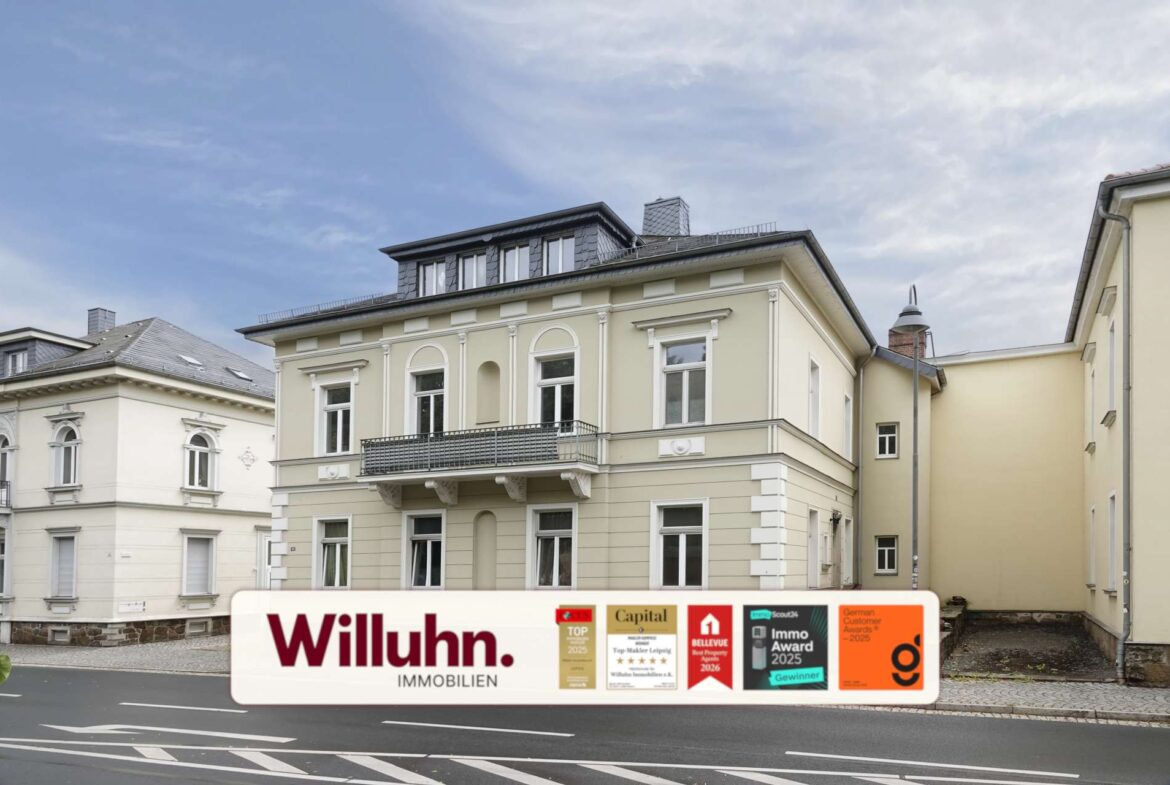 Beige, multi-story building on a city street with a large Willuhn Immobilien real estate sign and award stickers in front.
