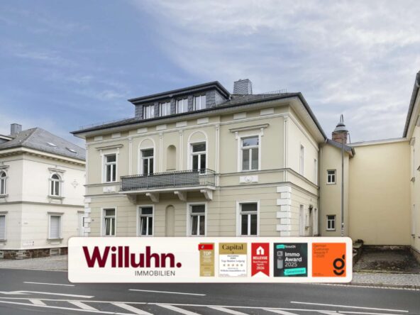 Beige, multi-story building on a city street with a large Willuhn Immobilien real estate sign and award stickers in front.