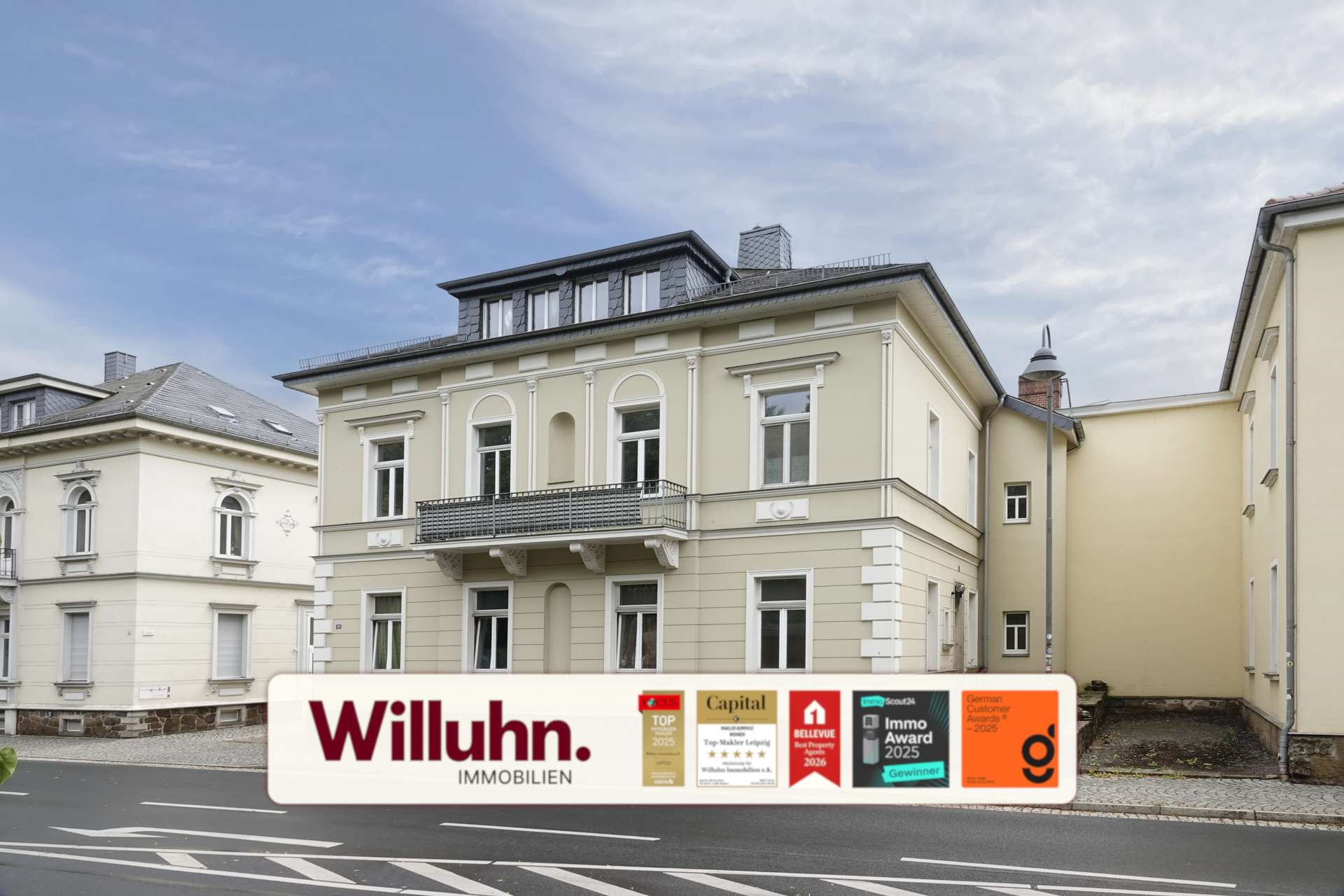 Beige, multi-story building on a city street with a large Willuhn Immobilien real estate sign and award stickers in front.