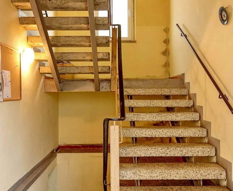 Concrete stairwell with yellow walls, metal railings, and a window at the landing—industrial building interior
