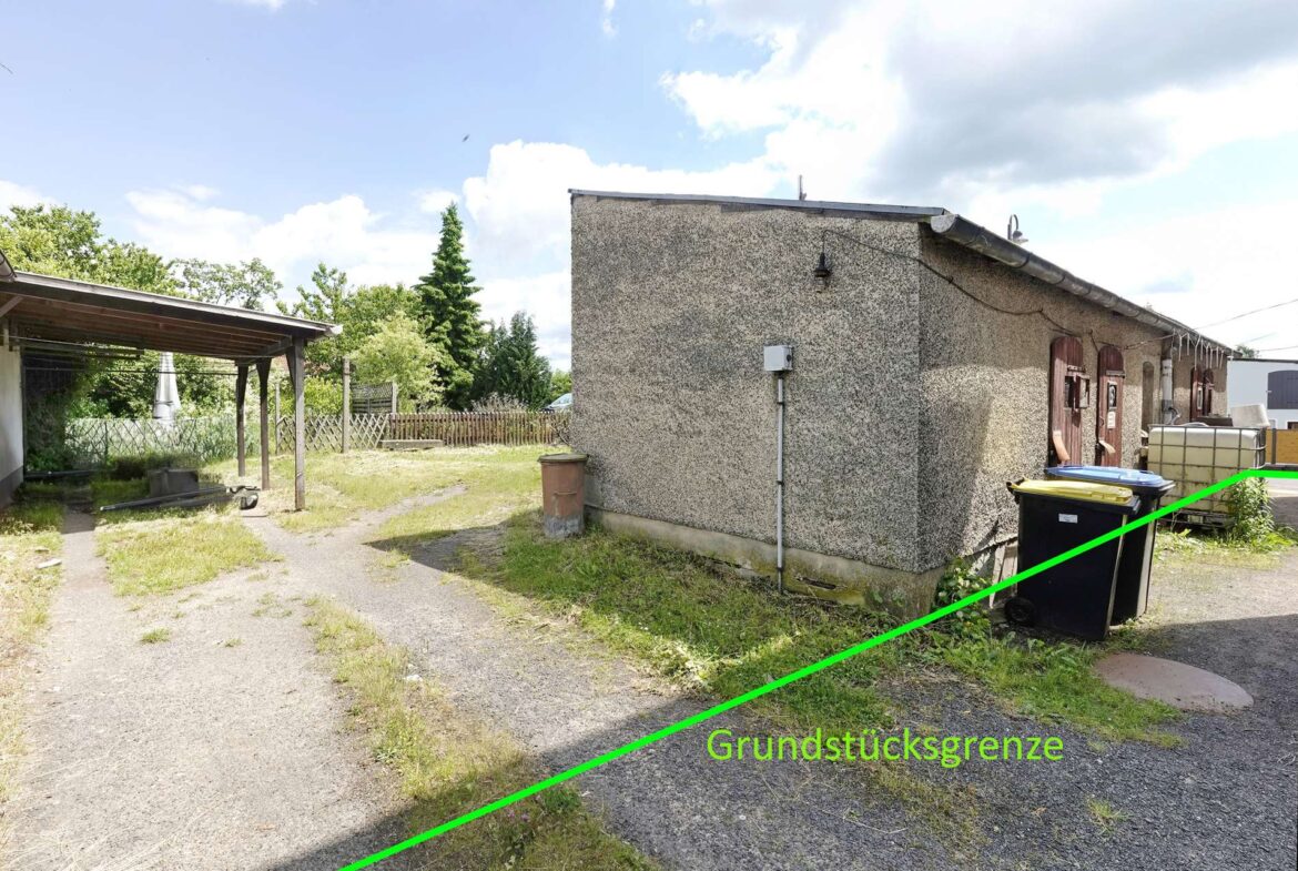 Side of a rough-textured building with a bright green diagonal line marking the property boundary and the label 'Grundstücksgrenze'