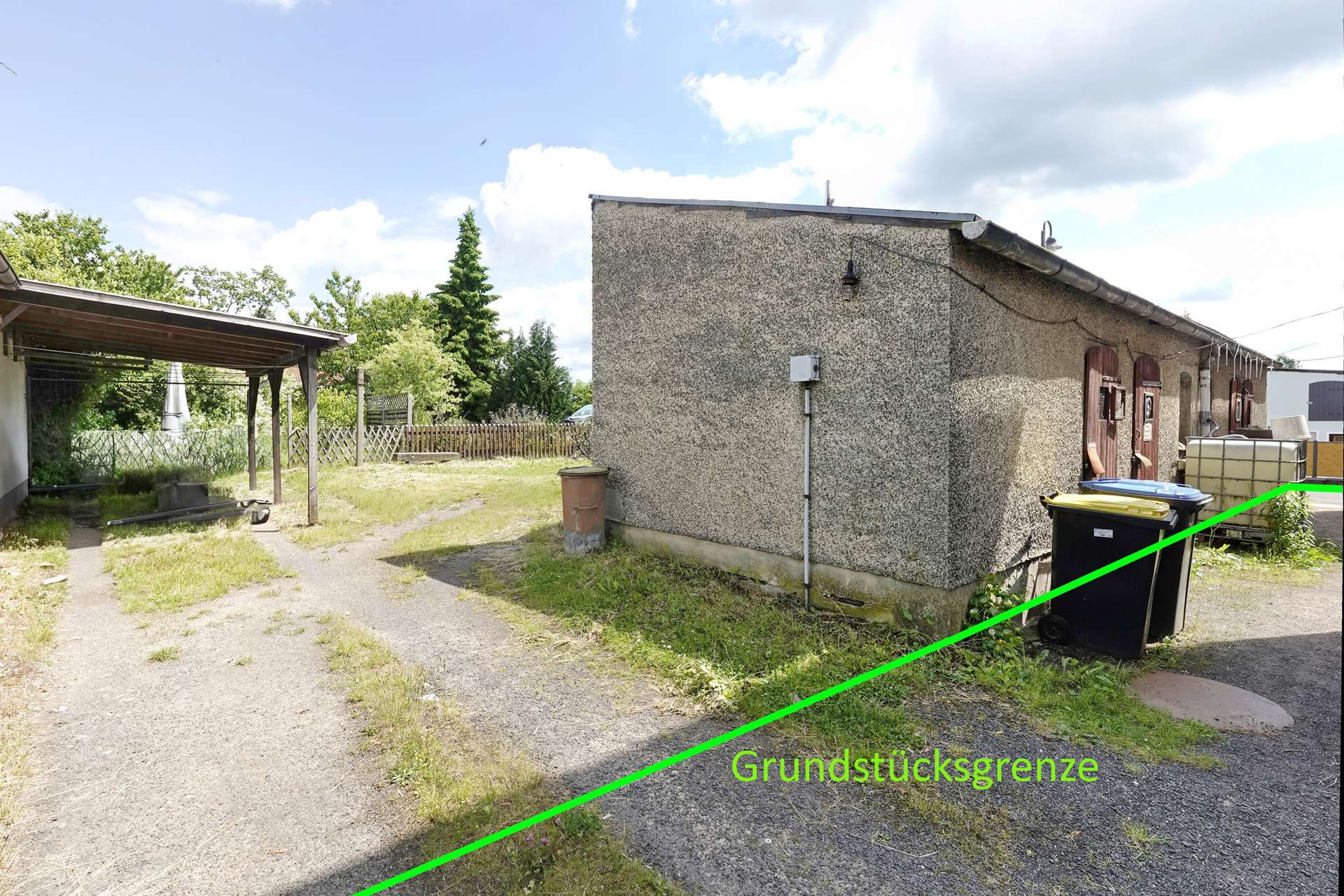 Side of a rough-textured building with a bright green diagonal line marking the property boundary and the label 'Grundstücksgrenze'