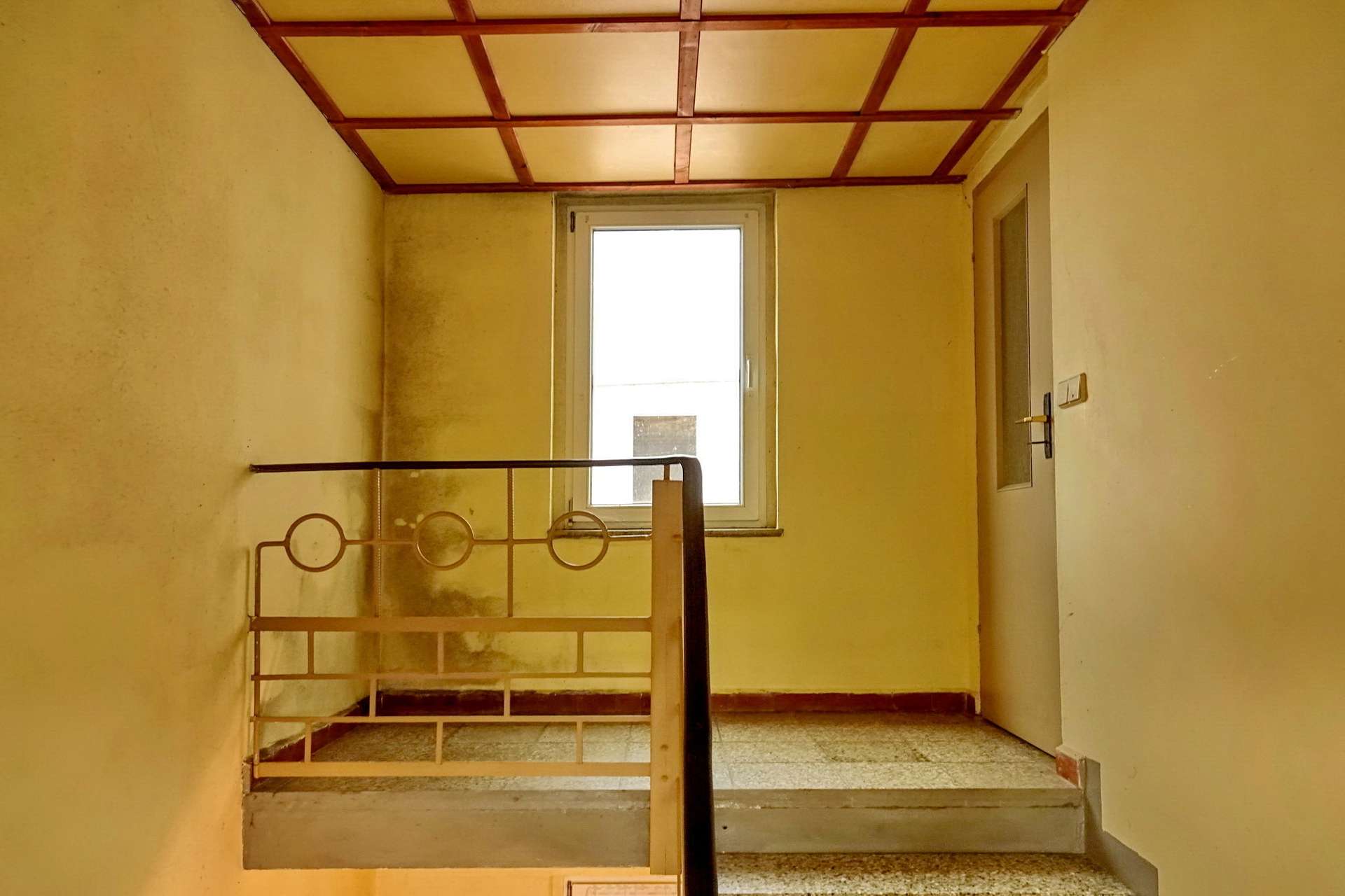 Interior stairwell with yellow walls, a metal railing, and a window at the landing.