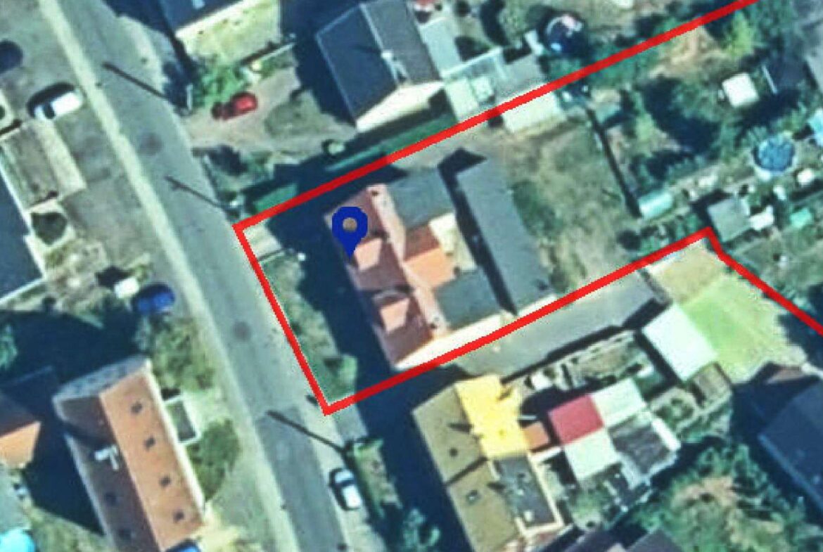 Aerial view of a house with red boundary lines marking its property, blue location pin at the center.