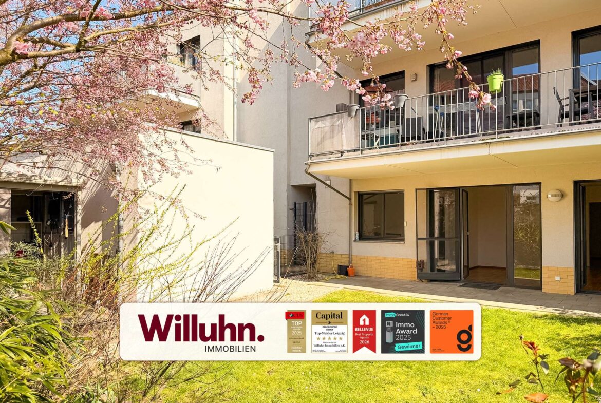 Apartment building with balconies and pink cherry blossoms in the foreground, featuring a Willuhn Immobilien sign on the lawn.
