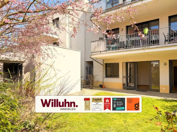 Apartment building with balconies and pink cherry blossoms in the foreground, featuring a Willuhn Immobilien sign on the lawn.