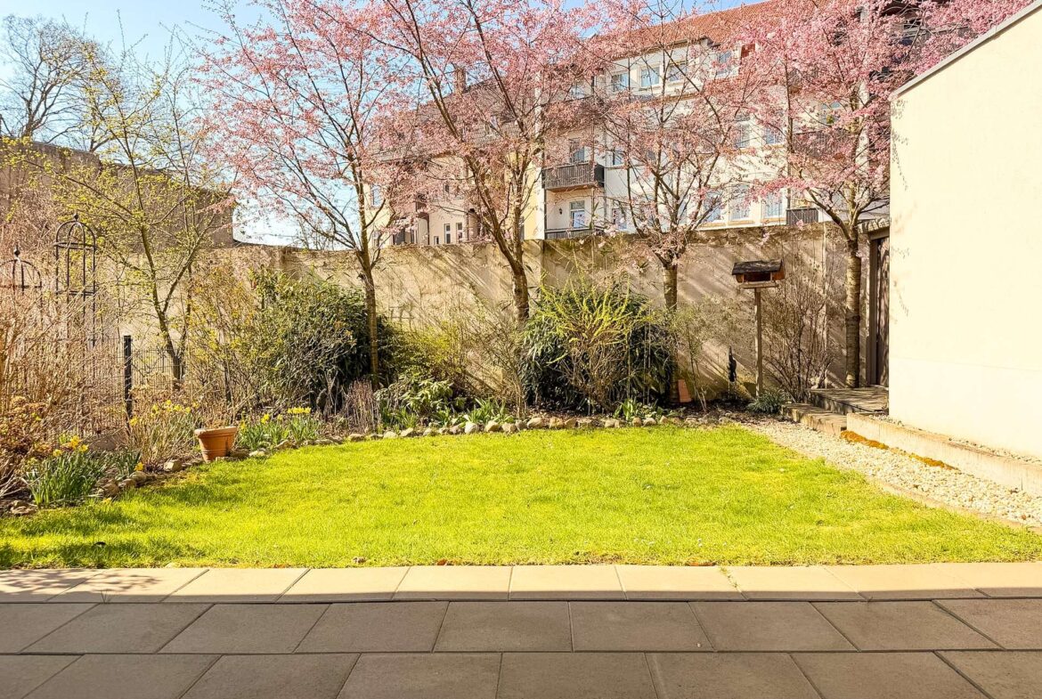 Courtyard garden with pink blossom trees and a green lawn, with a beige apartment building in the background.