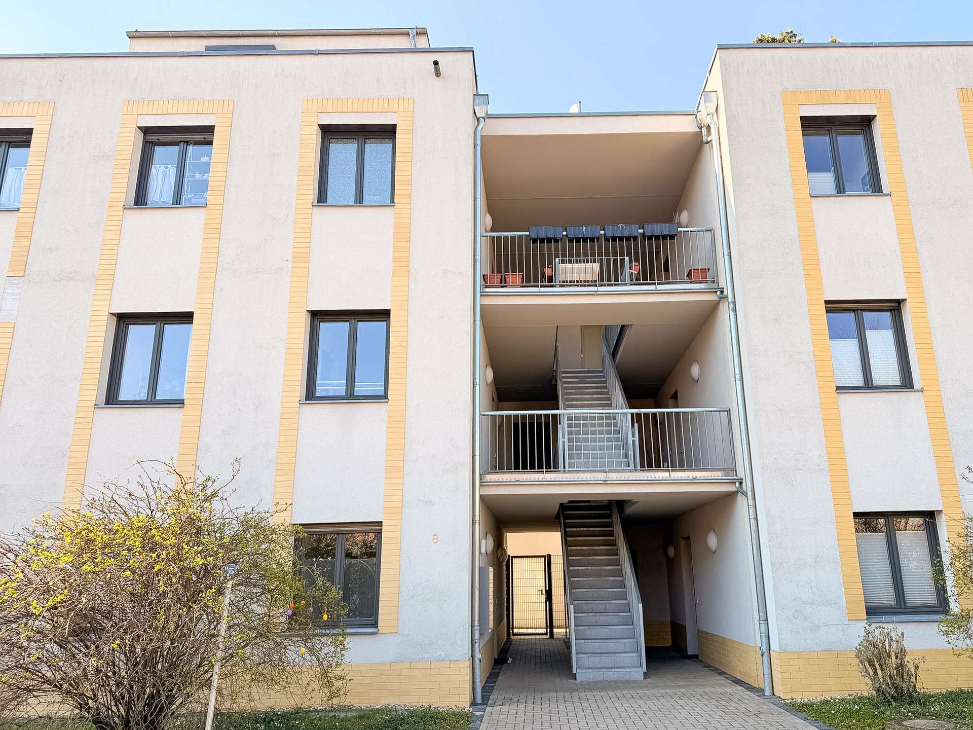 Facade of a beige apartment building with yellow trim and multiple windows, centered by an exterior stairwell and balcony area