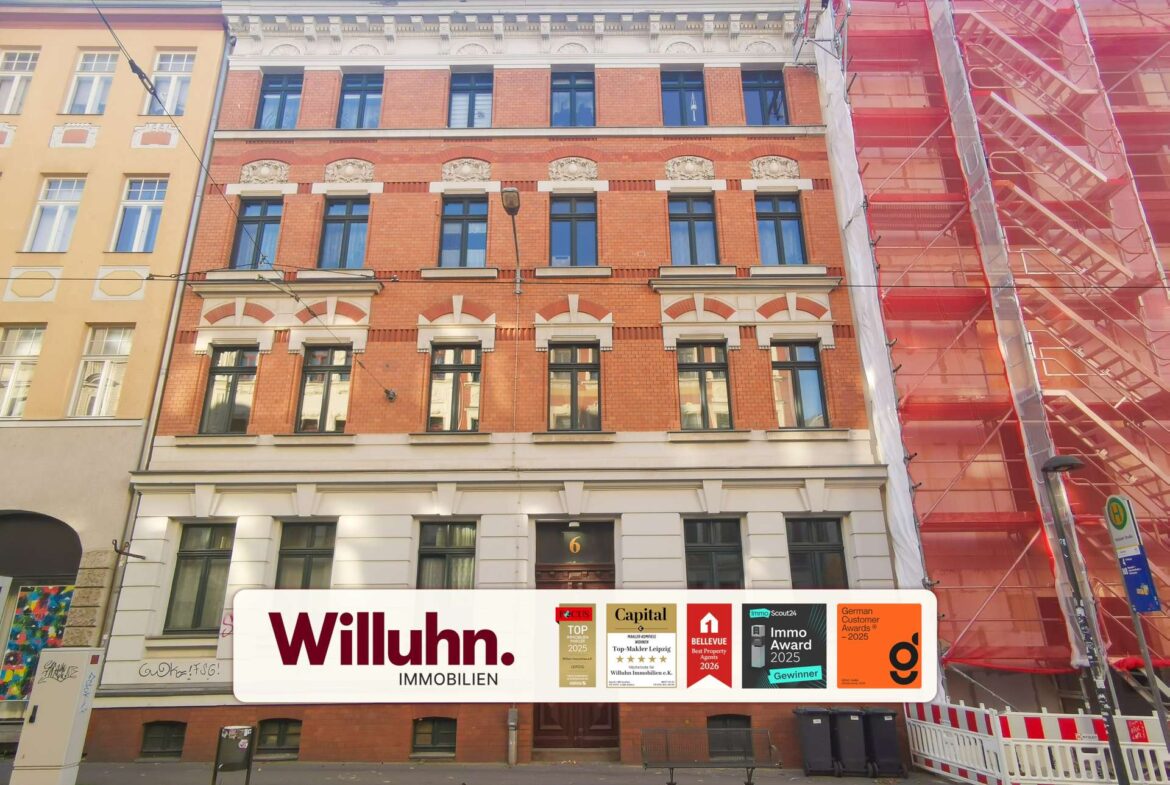 Red-brick mid-height building with ornate white decorative trim and tall windows, construction scaffolding wrapped in red netting on the right side.