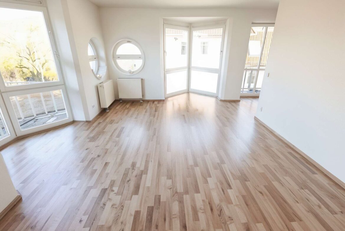Empty bright living room with light wood flooring and large bay window