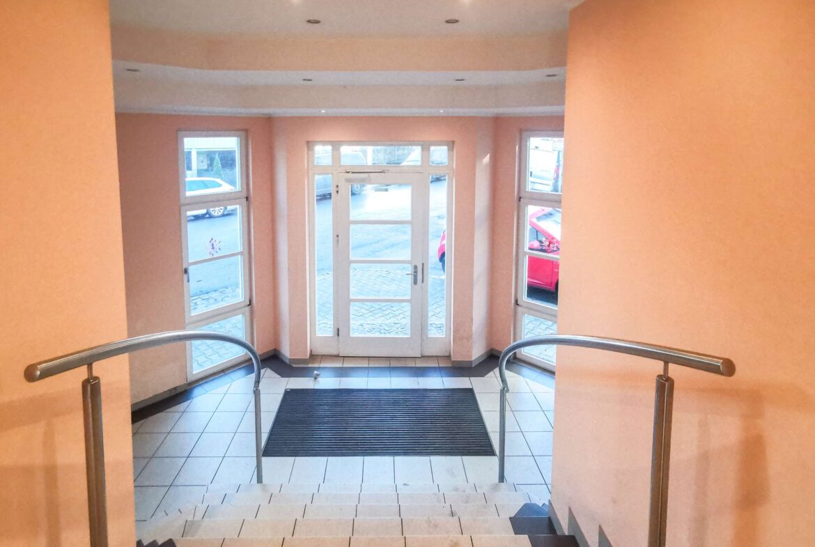 Interior stairwell leading down to glass double doors at entrance, peach walls and metal handrails on both sides