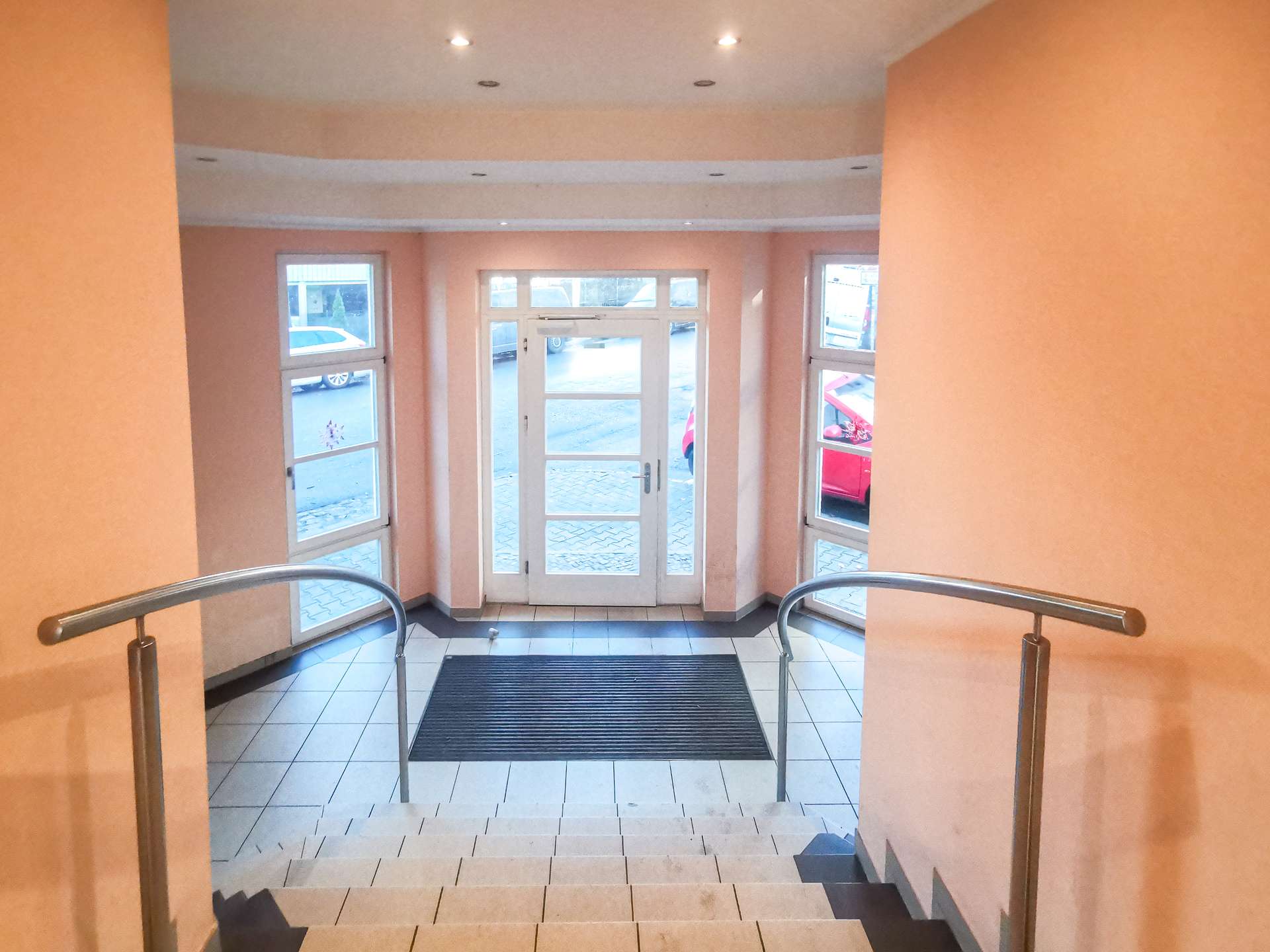 Interior stairwell leading down to glass double doors at entrance, peach walls and metal handrails on both sides