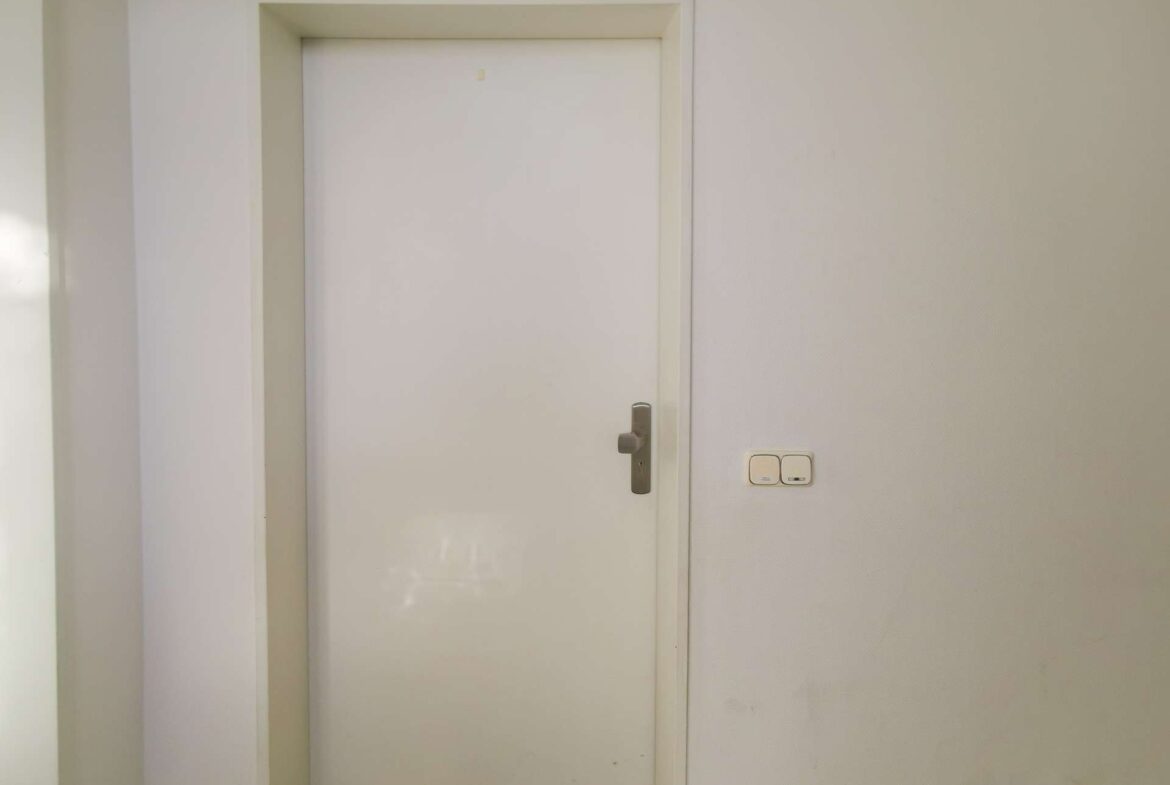 White interior door in a narrow hallway with a light switch on the wall to the right