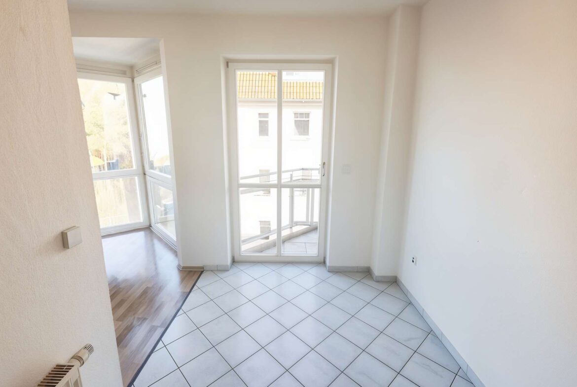 Bright corner room with large white-framed glass doors opening to a balcony, white walls and tiled floor.